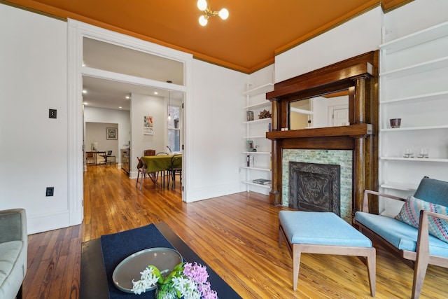 living room with baseboards, wood-type flooring, crown molding, and a tile fireplace