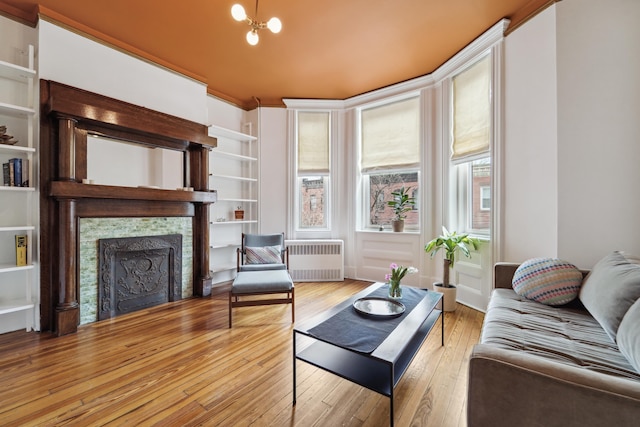 living area featuring a notable chandelier, radiator, hardwood / wood-style floors, and a tile fireplace