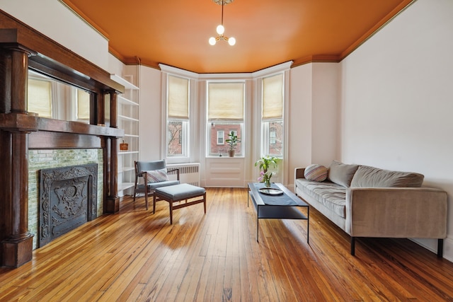 living area featuring radiator, hardwood / wood-style flooring, crown molding, and a tile fireplace