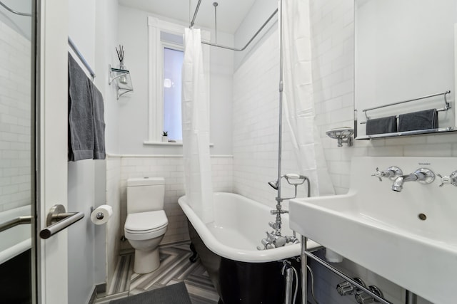 full bathroom with a sink, curtained shower, tile walls, toilet, and a bathtub