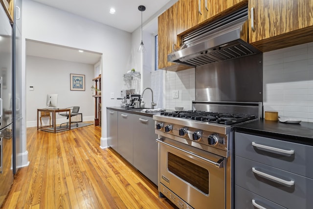 kitchen featuring a sink, extractor fan, light wood-style floors, dark countertops, and high quality appliances