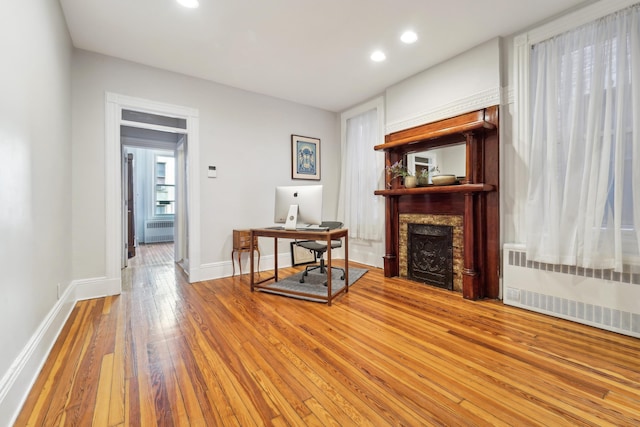 office featuring hardwood / wood-style floors, radiator, a fireplace, and baseboards