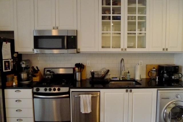 kitchen with a sink, washer / clothes dryer, dark countertops, stainless steel appliances, and white cabinets