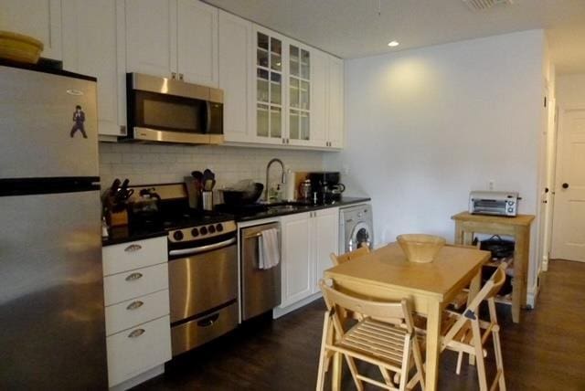 kitchen with washer / clothes dryer, dark countertops, appliances with stainless steel finishes, and white cabinetry