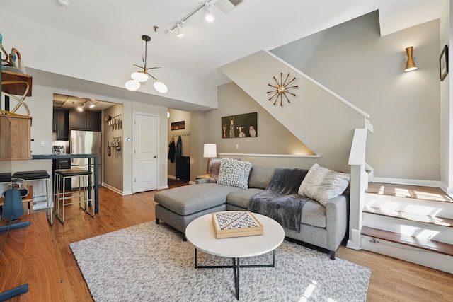 living area featuring lofted ceiling, track lighting, visible vents, light wood-style floors, and baseboards