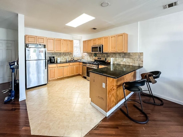 3481 John F Kennedy Blvd Unit 301, Jersey City, NJ 07307 - kitchen featuring appliances with stainless steel finishes, a peninsula, light brown cabinetry, and tasteful backsplash