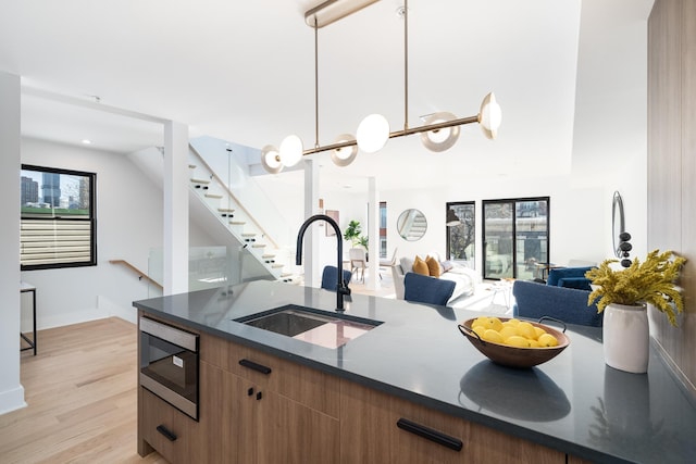 kitchen with built in microwave, sink, hanging light fixtures, dark stone counters, and light hardwood / wood-style floors