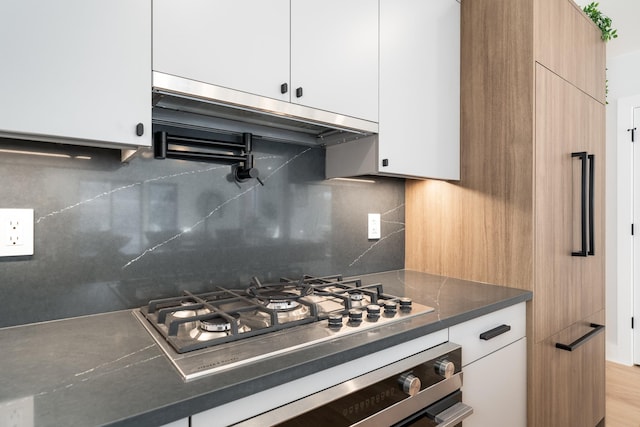 kitchen featuring appliances with stainless steel finishes, exhaust hood, white cabinets, and backsplash