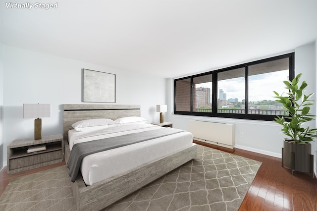 bedroom featuring a view of city, radiator heating unit, wood finished floors, and baseboards