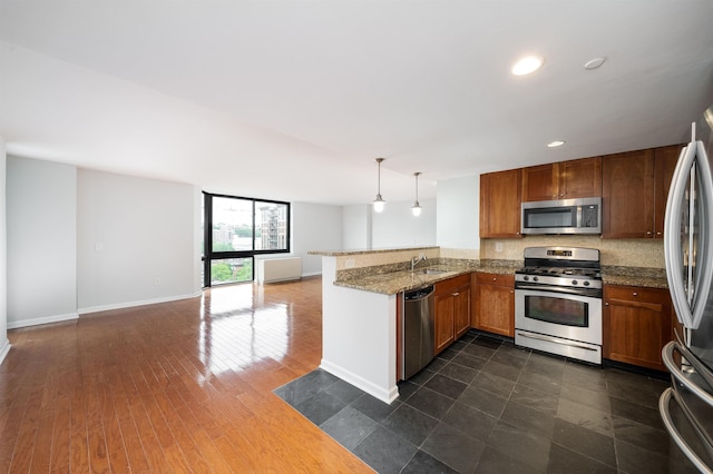 kitchen with dark wood-style floors, stainless steel appliances, brown cabinetry, open floor plan, and a peninsula