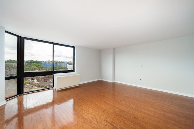 spare room with expansive windows, radiator, baseboards, and hardwood / wood-style floors