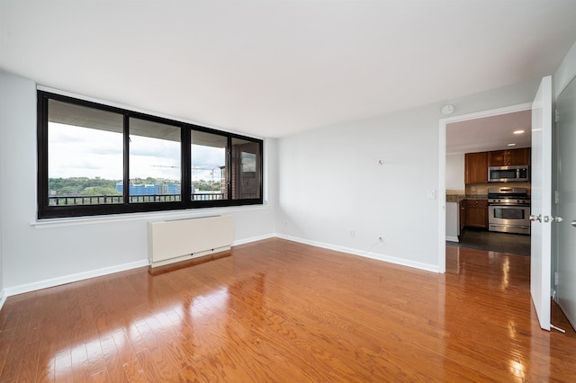 unfurnished room with baseboards, light wood-style flooring, and radiator heating unit