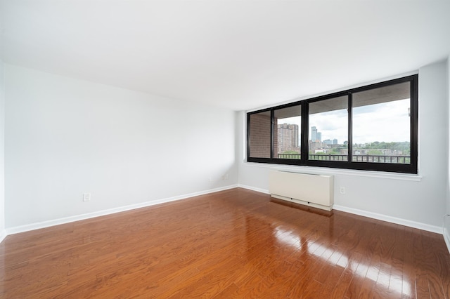 empty room with baseboards, a city view, wood-type flooring, and radiator