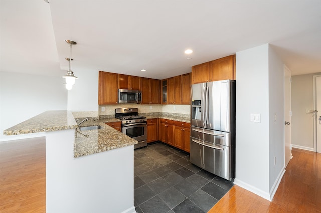 kitchen featuring light stone counters, stainless steel appliances, a peninsula, a sink, and brown cabinets