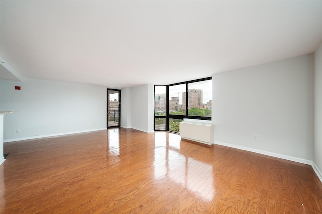 unfurnished living room featuring light wood-type flooring, floor to ceiling windows, a city view, and baseboards