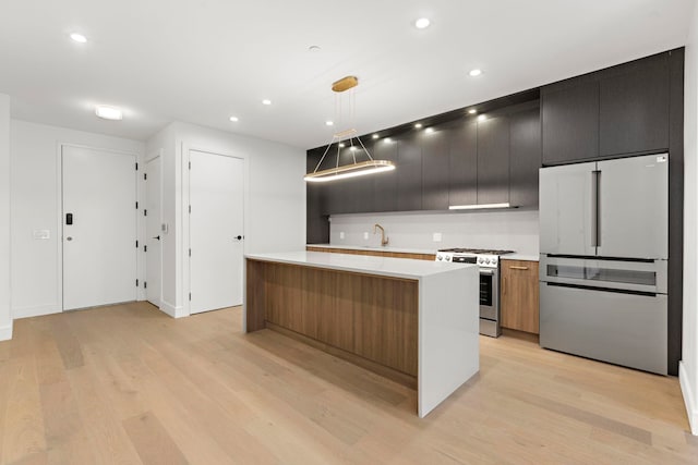 kitchen with a kitchen island, freestanding refrigerator, stainless steel gas range, light countertops, and light wood-style floors