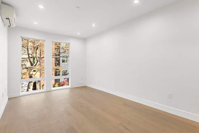 unfurnished room featuring light wood-style floors, recessed lighting, an AC wall unit, and baseboards