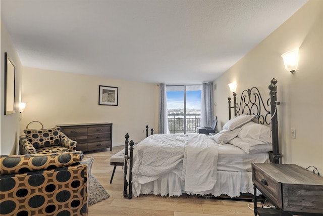 bedroom featuring access to exterior, light wood-type flooring, and a wall of windows