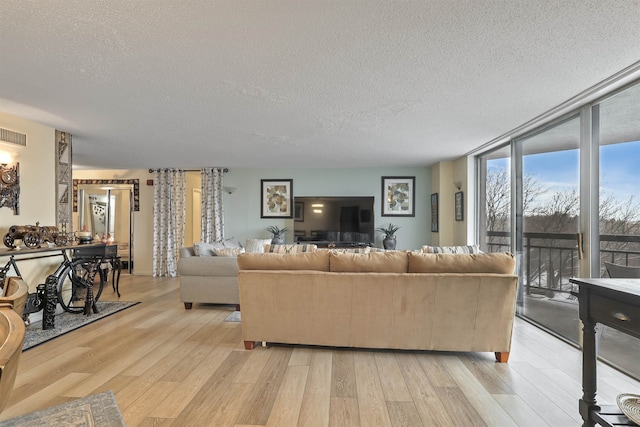 living room featuring light wood-type flooring, a textured ceiling, and a wall of windows