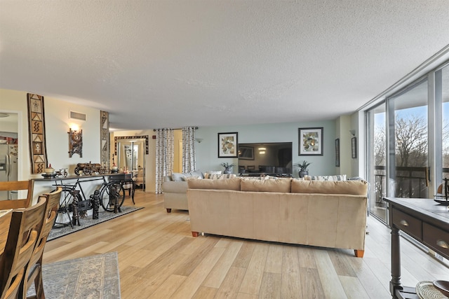 living room with light wood-type flooring, a wall of windows, and a textured ceiling