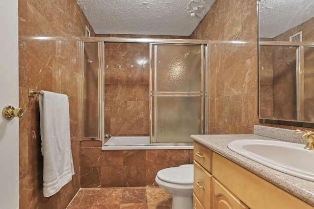 full bathroom featuring vanity, toilet, enclosed tub / shower combo, a textured ceiling, and tile walls