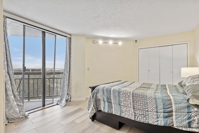 bedroom featuring access to exterior, expansive windows, light hardwood / wood-style floors, a textured ceiling, and a closet