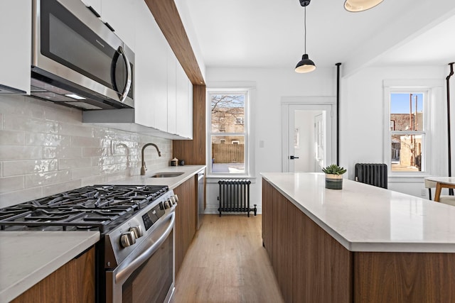 kitchen featuring sink, white cabinetry, appliances with stainless steel finishes, radiator, and pendant lighting