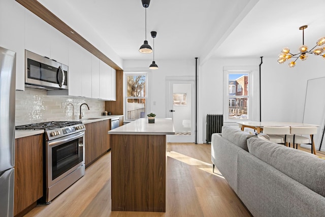 kitchen featuring sink, appliances with stainless steel finishes, a center island, white cabinets, and decorative light fixtures