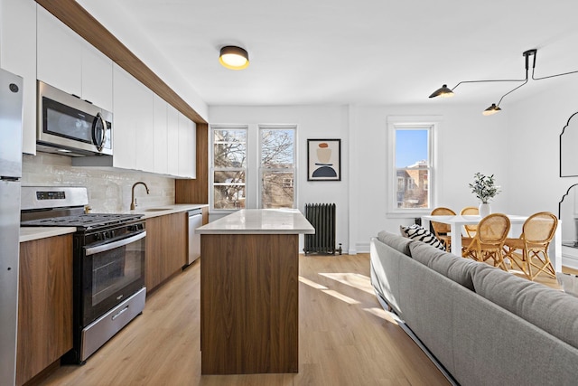 kitchen featuring radiator heating unit, white cabinetry, backsplash, a center island, and stainless steel appliances