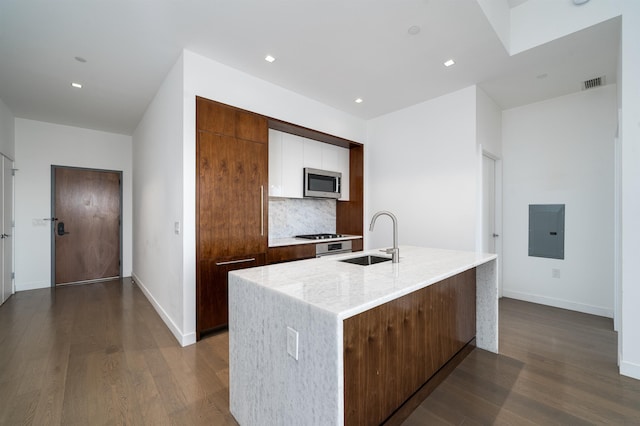 kitchen featuring sink, decorative backsplash, electric panel, dark wood-type flooring, and a center island with sink