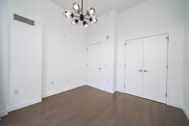 unfurnished bedroom featuring an inviting chandelier, a towering ceiling, dark hardwood / wood-style floors, and a closet