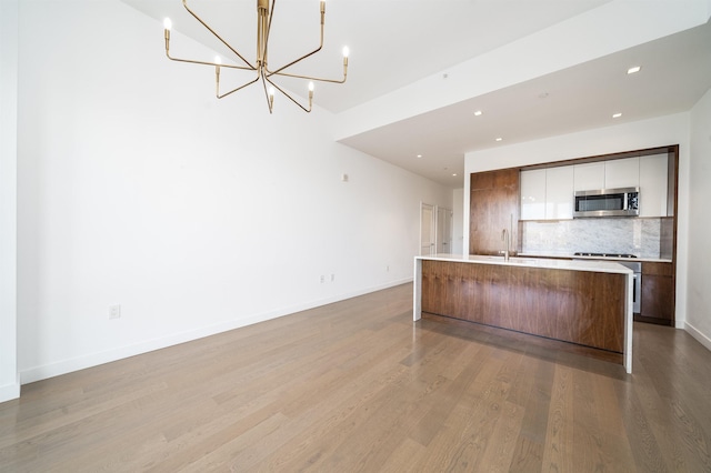 kitchen featuring gas stovetop, tasteful backsplash, light wood-type flooring, a notable chandelier, and a kitchen island with sink