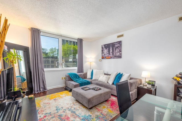 living area with wood finished floors, baseboards, a textured ceiling, and visible vents