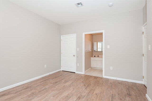 unfurnished bedroom featuring connected bathroom, baseboards, visible vents, and light wood finished floors