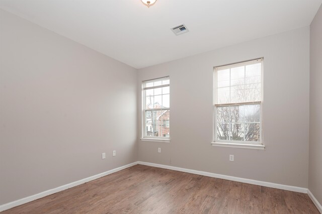 empty room featuring baseboards, wood finished floors, and visible vents