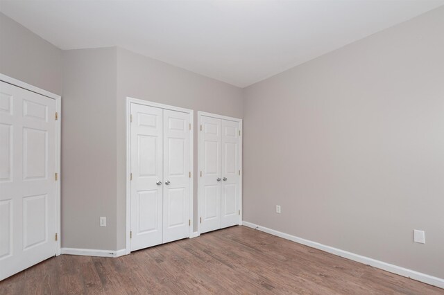 unfurnished bedroom featuring baseboards, two closets, and wood finished floors