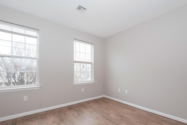 empty room featuring visible vents, baseboards, plenty of natural light, and wood finished floors