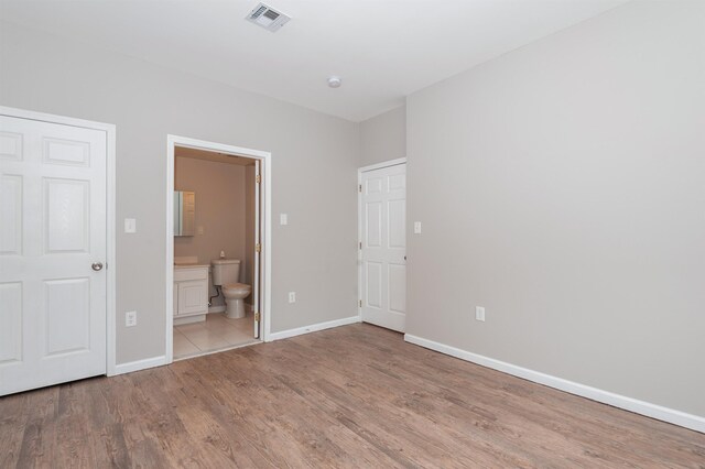 unfurnished bedroom with connected bathroom, baseboards, visible vents, and wood finished floors
