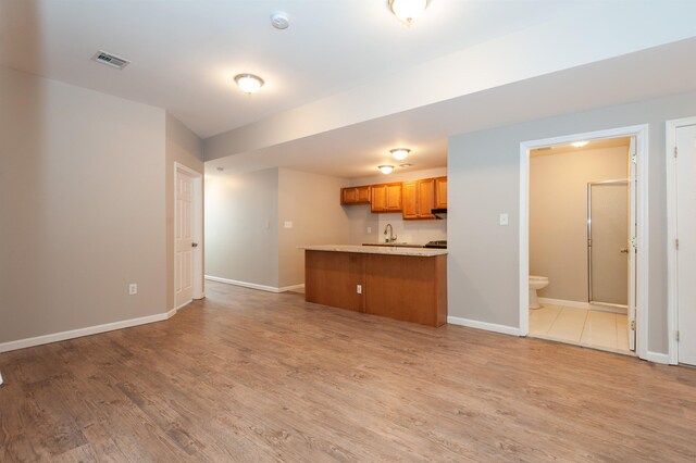 kitchen featuring brown cabinetry, a peninsula, baseboards, light countertops, and light wood-style flooring