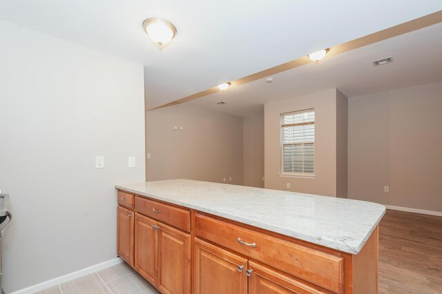 kitchen with light stone countertops, brown cabinetry, a peninsula, baseboards, and visible vents