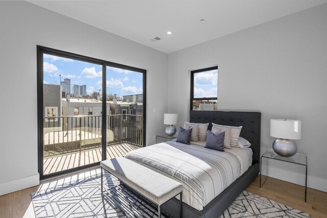 bedroom with access to exterior, a city view, multiple windows, and wood finished floors