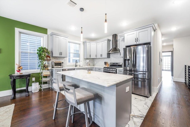 kitchen with a center island, stainless steel appliances, wall chimney range hood, backsplash, and decorative light fixtures