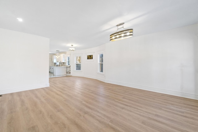 unfurnished living room with an inviting chandelier and light wood-type flooring