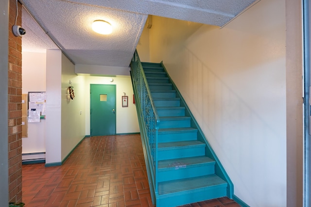 stairs featuring a textured ceiling, baseboard heating, brick floor, and baseboards