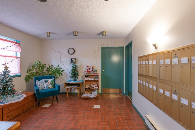 living area with baseboards, brick floor, mail area, a textured ceiling, and a baseboard heating unit