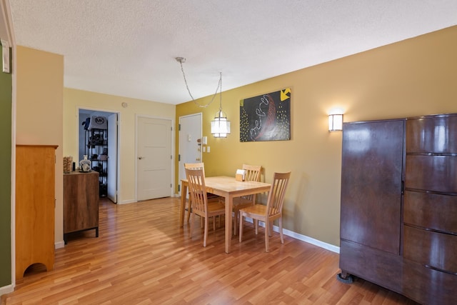 dining room featuring a textured ceiling, light wood-type flooring, and baseboards