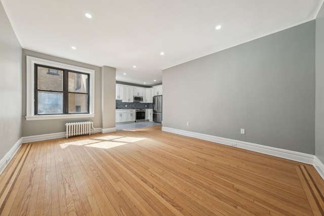 unfurnished living room featuring radiator heating unit, baseboards, light wood-style flooring, and recessed lighting