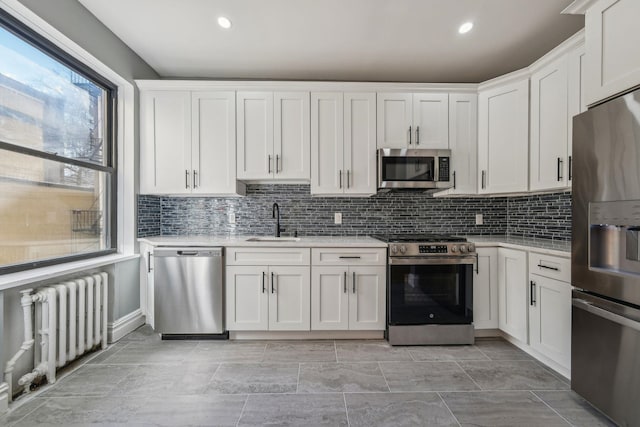 kitchen featuring decorative backsplash, white cabinets, radiator, appliances with stainless steel finishes, and a sink