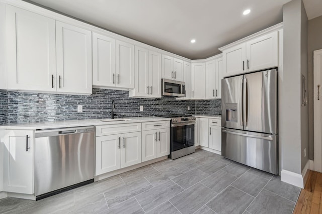 kitchen with stainless steel appliances, a sink, white cabinets, light countertops, and backsplash