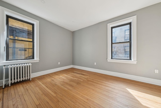 spare room with radiator heating unit, light wood-type flooring, and baseboards